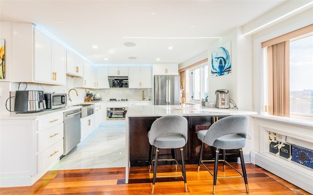 4318 Main St Unit 12A, Flushing, NY 11355 - kitchen with appliances with stainless steel finishes, a breakfast bar area, white cabinetry, light countertops, and decorative backsplash