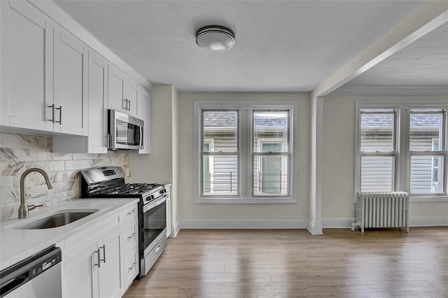 58-60 78th Ave, Glendale, NY 11385 - kitchen featuring appliances with stainless steel finishes, radiator, tasteful backsplash, light wood-style floors, and white cabinets