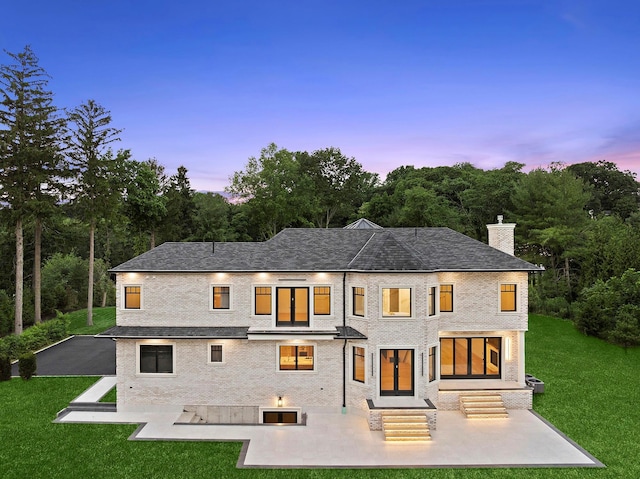26 Saint Andrews Ct, Old Westbury, NY 11568 - back of property at dusk with a patio area, a lawn, a chimney, and a shingled roof
