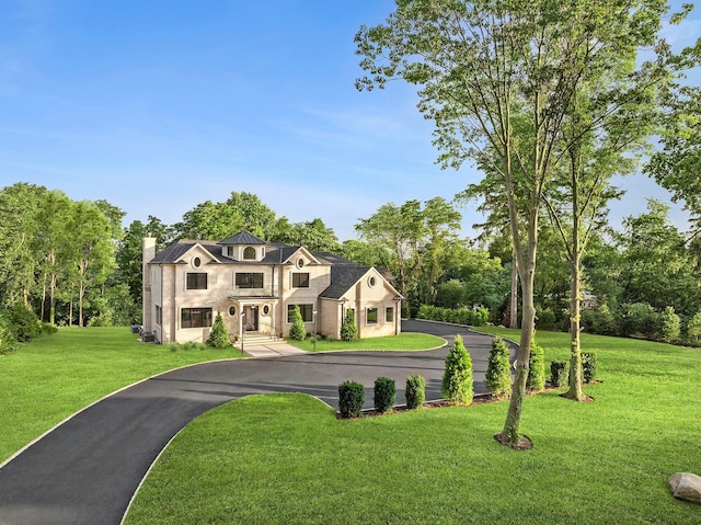 26 Saint Andrews Ct, Old Westbury, NY 11568 - view of front facade featuring a chimney, a front lawn, stucco siding, view of scattered trees, and asphalt driveway