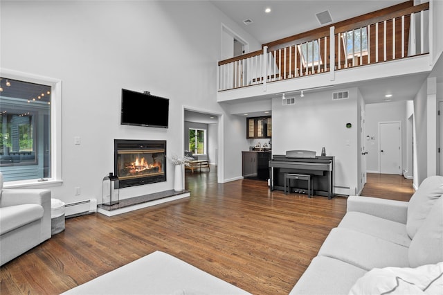 32 Pine Dr, Pound Ridge, NY 10576 - living room featuring a towering ceiling, a baseboard radiator, a glass covered fireplace, wood finished floors, and baseboard heating
