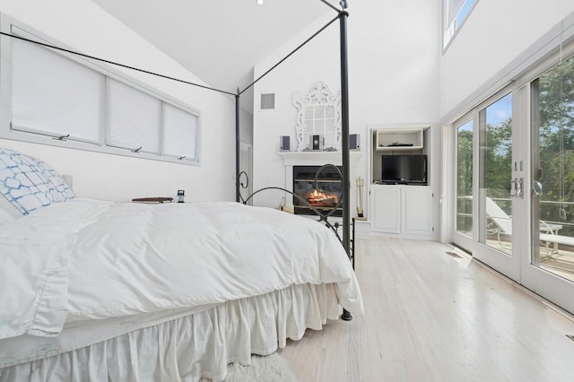 61 Hidden Cove Ct, Southampton, NY 11968 - bedroom with access to outside, light wood-style floors, a glass covered fireplace, and high vaulted ceiling
