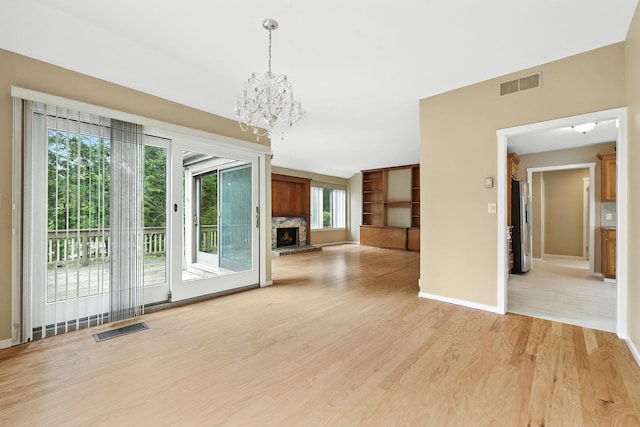 206 Heritage Unit A, Somers, NY 10589 - unfurnished room featuring a stone fireplace, a chandelier, built in shelves, and light wood-type flooring