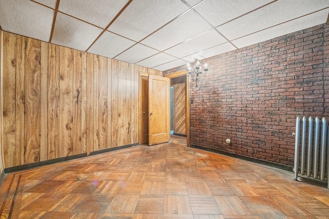 2117 38th St, Astoria, NY 11105 - unfurnished room with radiator heating unit, a drop ceiling, brick wall, and wood walls