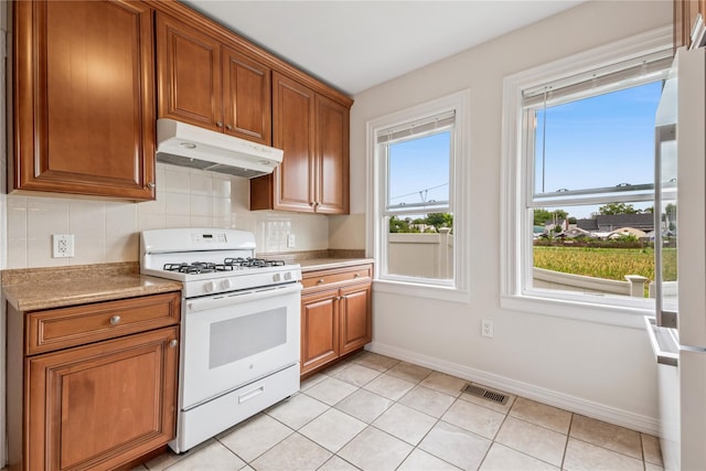 401 Ocean Ave, Malverne, NY 11565 - kitchen with white gas range oven, under cabinet range hood, backsplash, and brown cabinets