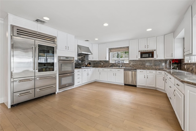230 W Beech St, Long Beach, NY 11561 - kitchen featuring built in appliances, wall chimney range hood, white cabinets, tasteful backsplash, and recessed lighting