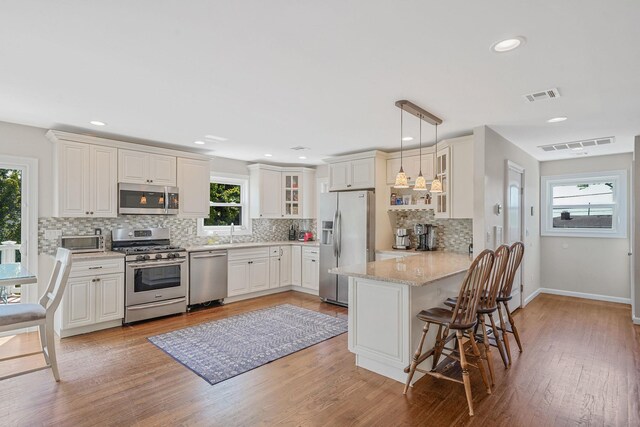 43 E Jackson Ave, Babylon, NY 11702 - kitchen featuring appliances with stainless steel finishes, a peninsula, glass insert cabinets, decorative backsplash, and a kitchen bar