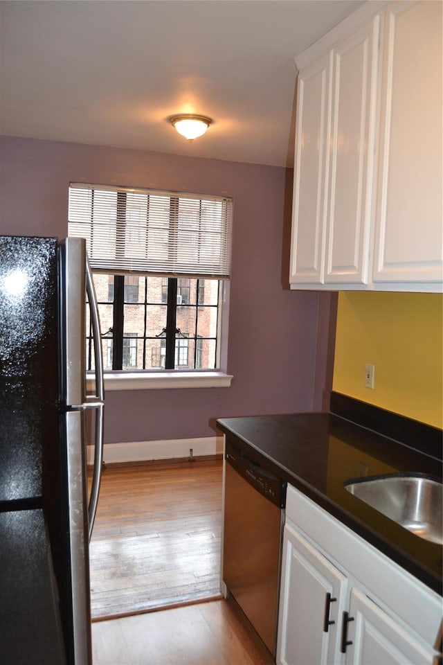 292 Main St Unit 4C, White Plains, NY 10601 - kitchen with freestanding refrigerator, stainless steel dishwasher, dark countertops, white cabinetry, and light wood-type flooring