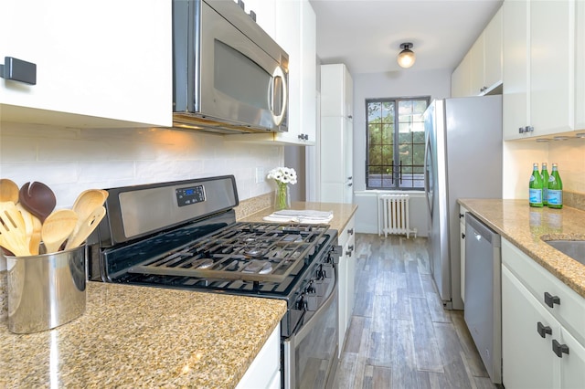 914 Wynnewood Rd Unit 3R, Pelham, NY 10803 - kitchen featuring appliances with stainless steel finishes, radiator, backsplash, white cabinets, and light wood-style floors