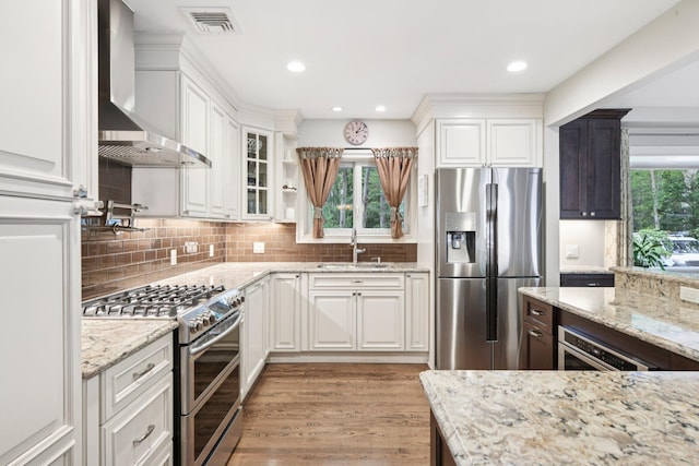 23 Alpine Way S, Huntington, NY 11746 - kitchen featuring appliances with stainless steel finishes, wall chimney exhaust hood, white cabinetry, light stone counters, and light wood-type flooring