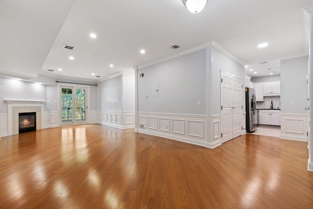 257 Central Ave Unit 1D, White Plains, NY 10606 - unfurnished living room featuring a decorative wall, crown molding, light wood finished floors, a glass covered fireplace, and wainscoting