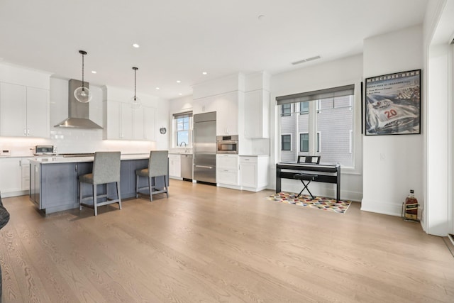 720 Davenport Ave Unit 3, New Rochelle, NY 10805 - kitchen featuring wall chimney range hood, appliances with stainless steel finishes, white cabinets, decorative backsplash, and light wood-style floors