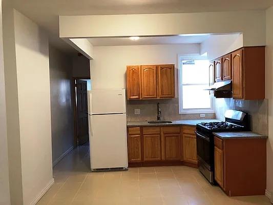 31-67 44th St, Astoria, NY 11103 - kitchen with freestanding refrigerator, black gas range oven, brown cabinetry, and decorative backsplash