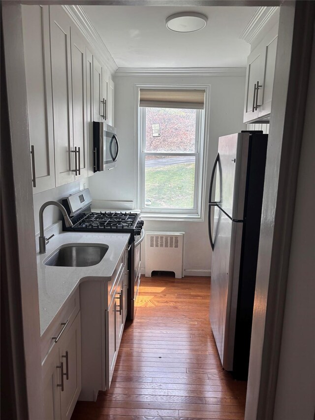 1133 Midland Ave Unit 1K, Yonkers, NY 10708 - kitchen with stainless steel appliances, radiator heating unit, ornamental molding, hardwood / wood-style floors, and light stone countertops