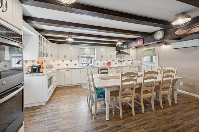 123 Pleasant Rd, Lake Peekskill, NY 10537 - kitchen with a wall mounted air conditioner, tasteful backsplash, stainless steel double oven, white cabinets, and beamed ceiling