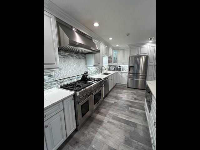29 Erin Ln Unit 29, East Setauket, NY 11733 - kitchen with appliances with stainless steel finishes, exhaust hood, light stone countertops, backsplash, and white cabinetry