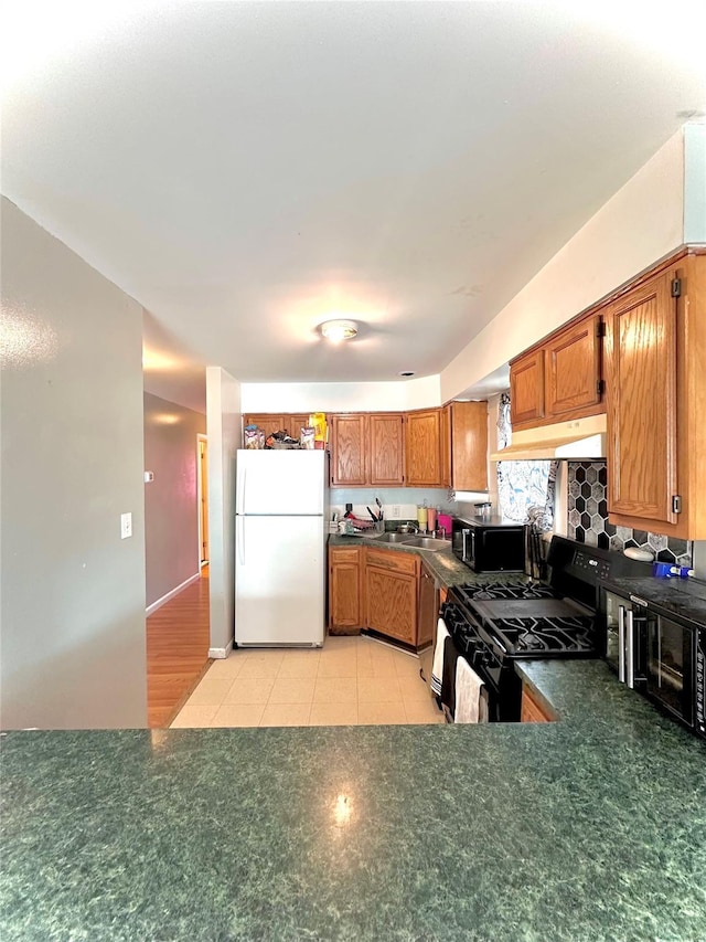 37 E Fulton St, Lido Beach, NY 11561 - kitchen featuring black appliances, under cabinet range hood, dark countertops, brown cabinetry, and light tile patterned floors