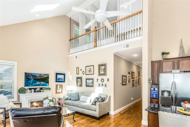 122 Maya Cir, Central Islip, NY 11722 - living room with high vaulted ceiling, light wood-type flooring, ceiling fan, a skylight, and a warm lit fireplace