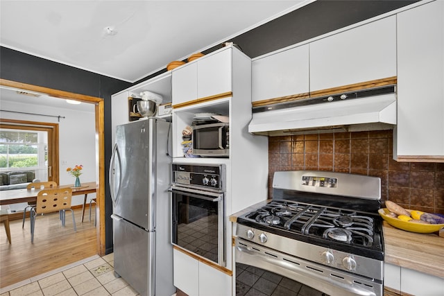 7641 N Broadway, Red Hook, NY 12571 - kitchen featuring appliances with stainless steel finishes, under cabinet range hood, white cabinets, light tile patterned floors, and decorative backsplash