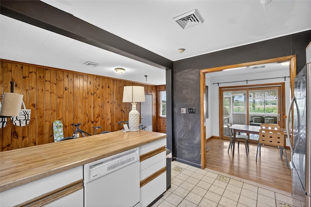 7641 N Broadway, Red Hook, NY 12571 - kitchen featuring white dishwasher, light tile patterned floors, stainless steel refrigerator, white cabinets, and wood walls