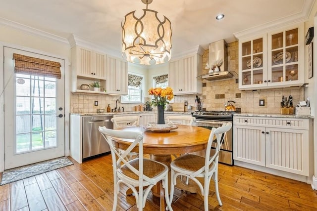 369 S 16th St, Lindenhurst, NY 11757 - kitchen featuring stainless steel appliances, wall chimney range hood, light wood finished floors, ornamental molding, and a chandelier