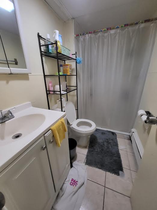 22 Prospect Ave, Brentwood, NY 11717 - bathroom with tile patterned flooring, vanity, baseboard heating, and a shower with shower curtain