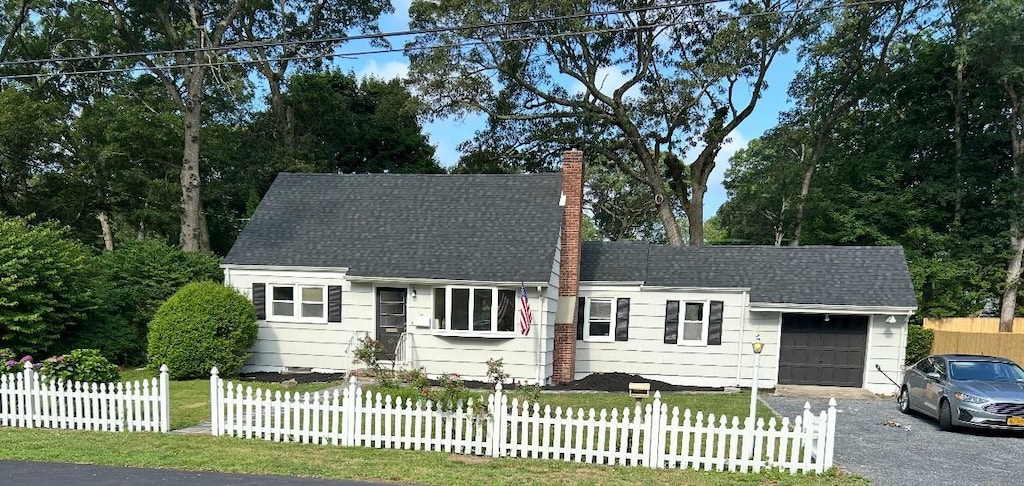 12 William St, Port Jefferson Station, NY 11776 - cape cod home with a chimney, an attached garage, a fenced front yard, driveway, and a shingled roof