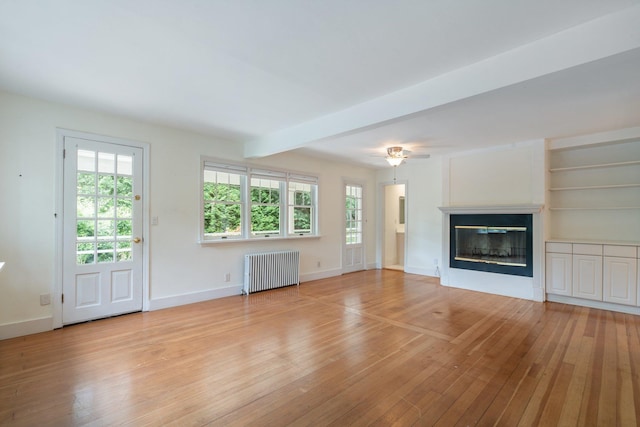 1459 N Country Rd, Wading River, NY 11792 - unfurnished living room with radiator heating unit, light wood-style flooring, a glass covered fireplace, and a ceiling fan