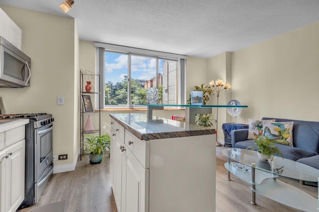 345 E 93rd St Unit 2E, New York Manhattan, NY 10128 - kitchen featuring appliances with stainless steel finishes, light wood finished floors, white cabinetry, a textured ceiling, and a kitchen island
