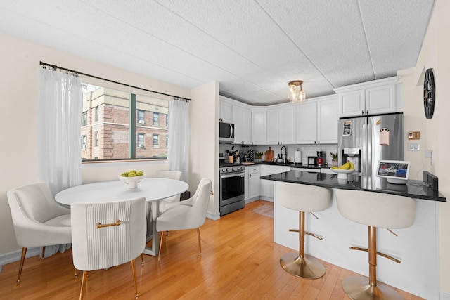 3220 Fairfield Ave Unit 6A, Bronx, NY 10463 - kitchen featuring appliances with stainless steel finishes, white cabinets, light wood finished floors, dark countertops, and a kitchen bar