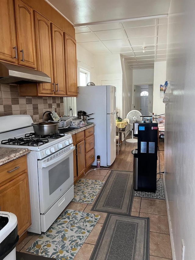 9414 125th St, Richmond Hill, NY 11419 - kitchen with white appliances, under cabinet range hood, brown cabinetry, decorative backsplash, and light stone counters