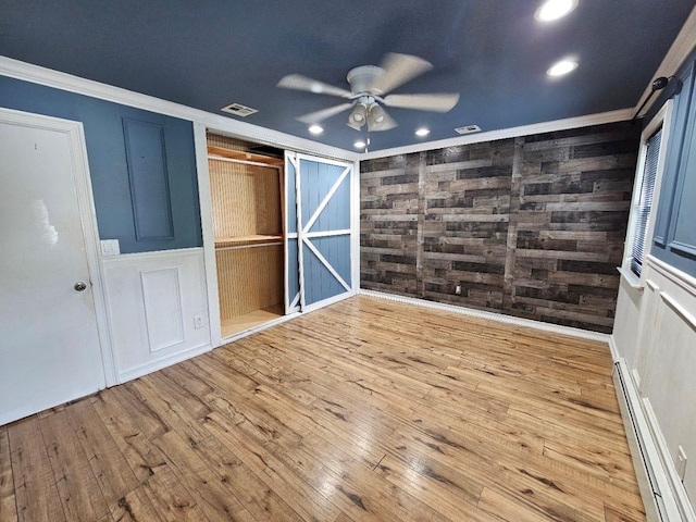 143 N Summit Ave, Patchogue, NY 11772 - unfurnished bedroom featuring baseboard heating, crown molding, hardwood / wood-style floors, wooden walls, and a closet