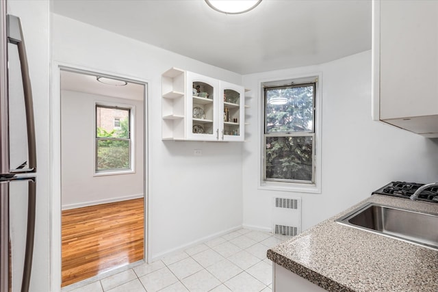 67-30 Clyde St Unit 3L, Forest Hills, NY 11375 - kitchen featuring white cabinets, open shelves, radiator, light tile patterned floors, and glass insert cabinets