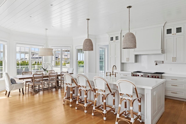1 Fiske Ave, Westhampton Beach, NY 11978 - kitchen with light countertops, a kitchen island with sink, light wood-style floors, a breakfast bar, and ornamental molding