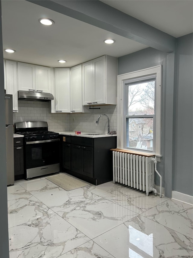68 Ramapo Rd, Garnerville, NY 10923 - kitchen with stainless steel gas range, radiator, decorative backsplash, white cabinetry, and under cabinet range hood