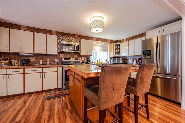 137 Jefferson St, Inwood, NY 11096 - kitchen featuring appliances with stainless steel finishes, light wood-type flooring, white cabinets, and a breakfast bar area