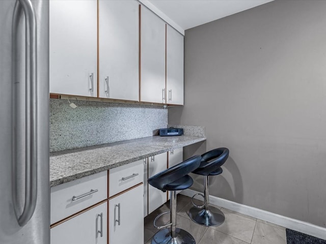 42-30 Douglaston Pkwy Unit 3L, Douglaston, NY 11363 - kitchen featuring stainless steel refrigerator, tasteful backsplash, built in study area, light tile patterned floors, and white cabinets
