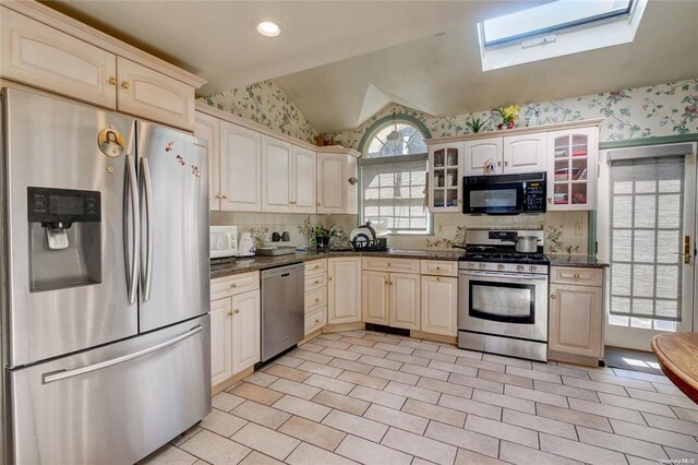 121 6th St, Hicksville, NY 11801 - kitchen featuring stainless steel appliances, a skylight, wallpapered walls, vaulted ceiling, and glass insert cabinets