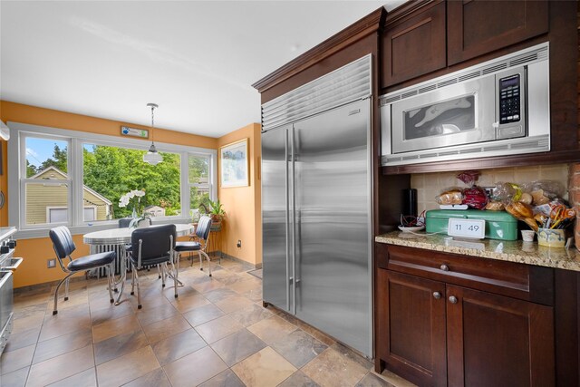 27 Neulist Ave, Port Washington, NY 11050 - kitchen with built in appliances, decorative light fixtures, light stone counters, dark brown cabinets, and decorative backsplash