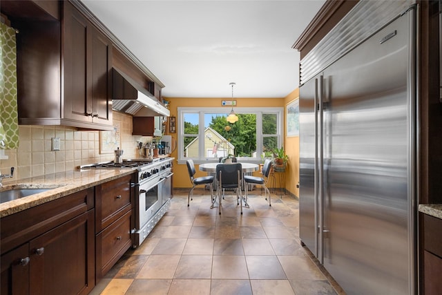 27 Neulist Ave, Port Washington, NY 11050 - kitchen with premium appliances, tasteful backsplash, dark brown cabinetry, light stone counters, and decorative light fixtures