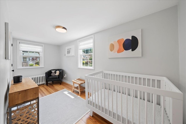56 Summers St, Oyster Bay, NY 11771 - bedroom with radiator, wood finished floors, a crib, and a wall mounted air conditioner