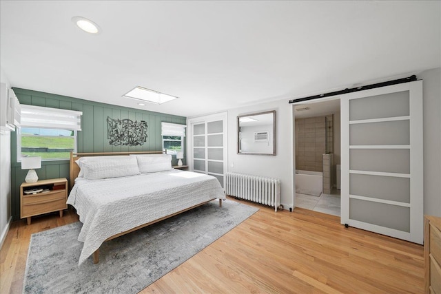 56 Summers St, Oyster Bay, NY 11771 - bedroom with radiator heating unit, a skylight, light wood finished floors, a barn door, and ensuite bath