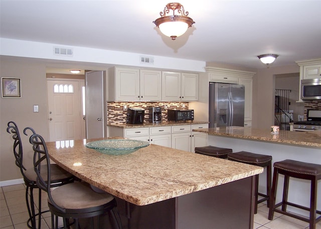 13 Lark Dr, Centereach, NY 11720 - kitchen with stainless steel appliances, light tile patterned floors, a breakfast bar, backsplash, and light stone counters