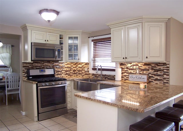 13 Lark Dr, Centereach, NY 11720 - kitchen with appliances with stainless steel finishes, a peninsula, light tile patterned floors, a breakfast bar area, and light stone countertops