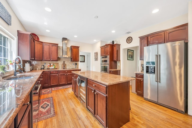 212A Lower Sheep Pasture Rd, East Setauket, NY 11733 - kitchen featuring stainless steel appliances, wall chimney range hood, a center island, light wood-style floors, and light stone countertops