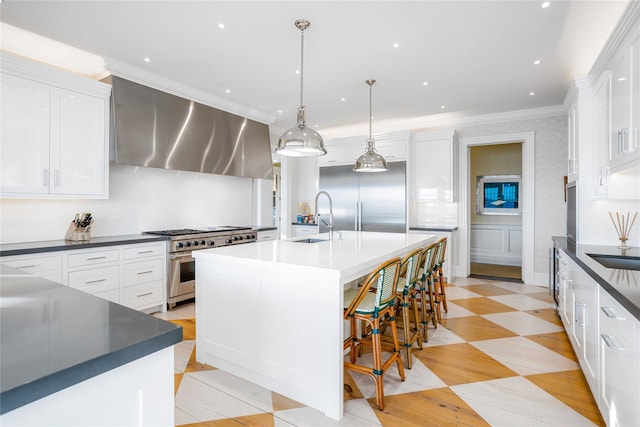 59 Shore Rd, Westhampton, NY 11977 - kitchen featuring high end appliances, wall chimney exhaust hood, an island with sink, dark countertops, and white cabinetry