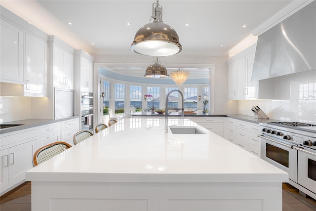 59 Shore Rd, Westhampton, NY 11977 - kitchen featuring range with two ovens, white cabinetry, light countertops, wall chimney range hood, and a kitchen island with sink