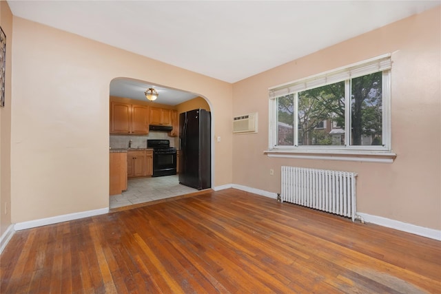 75-06A 255th St Unit A, Glen Oaks, NY 11004 - unfurnished living room with radiator, arched walkways, light wood-style flooring, and a wall mounted AC