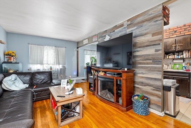 51-23 71st St, Woodside, NY 11377 - living room featuring light wood-style flooring, a baseboard heating unit, an accent wall, a fireplace, and wood walls