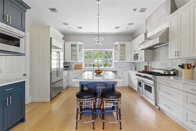 12 N Rd, Laurel Hollow, NY 11771 - kitchen with built in appliances, wall chimney exhaust hood, light wood-type flooring, glass insert cabinets, and recessed lighting